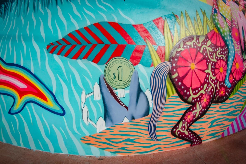 Detalhe do muram por Aaron Glasson, mostrando um golfinho cercado, com uma moeda de dinheiro na boca.