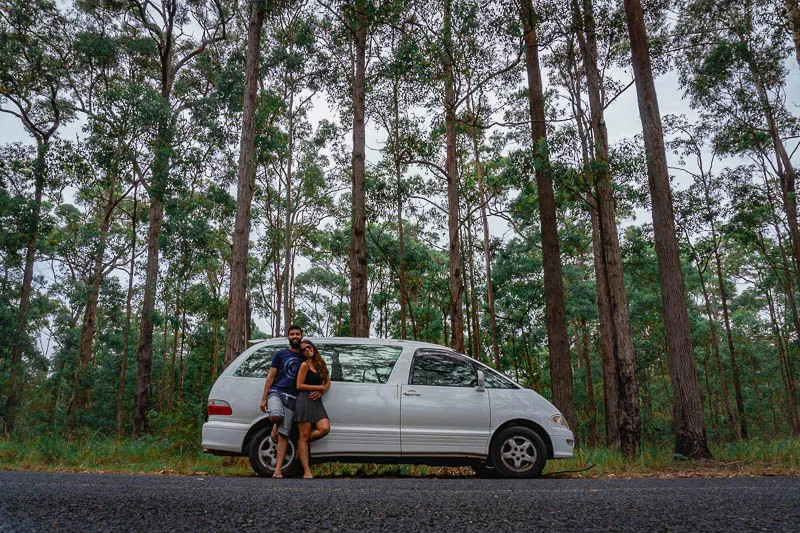 Casal em frente a campervan dirigindo por estrada cercada por árvores