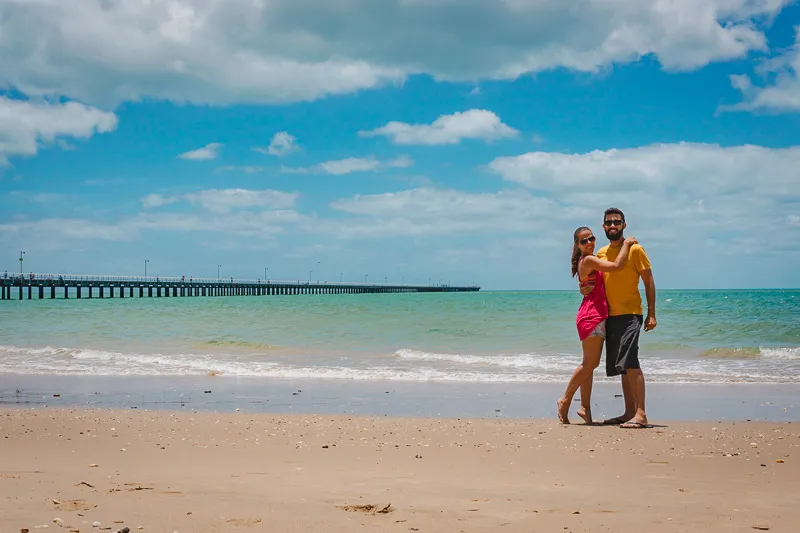 Casal em frente à praia de Hervey Bay, com pier ao fundo