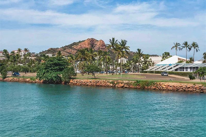 Vista da costa de Townsville, na Austrália, com mar azul, palmeiras e construções à beira-mar.
