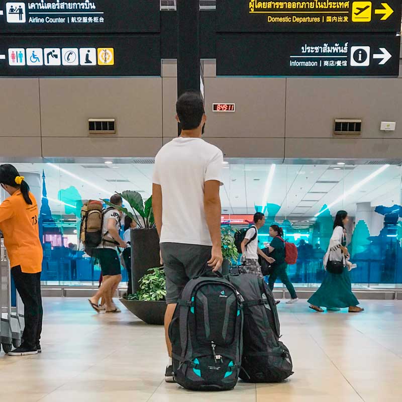 o que levar na mala de viagem? - viajante com 2 mochilões olhando painel no aeroporto