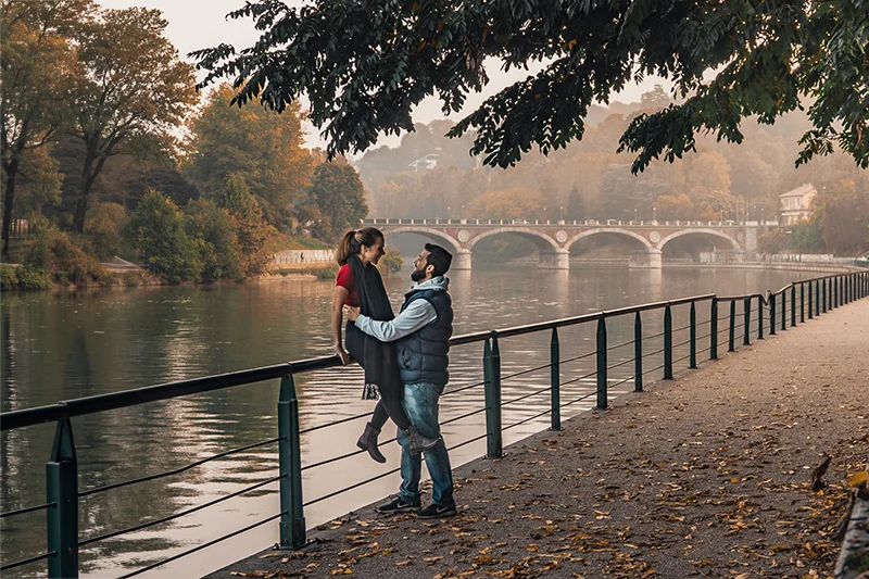 Casal abraçado diante de um lago em um parque na Europa, durante uma viagem no outono.